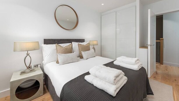 A modern hotel room with a large bed, two bedside tables, a mirror, and a wardrobe.