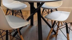 A dining area with a round table, four white chairs, a bowl, and a pendant light.