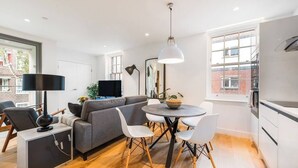 A modern living space with a grey sofa, white chairs, a round dining table, and a black lamp.