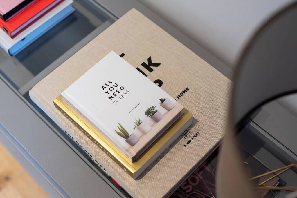 A book titled 'All You Need is Less' by Vicki Vigne on a shelf with a beige background and a small plant illustration.