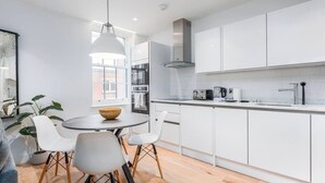 A modern kitchen with white cabinets, a round dining table with chairs, and a hanging light fixture.
