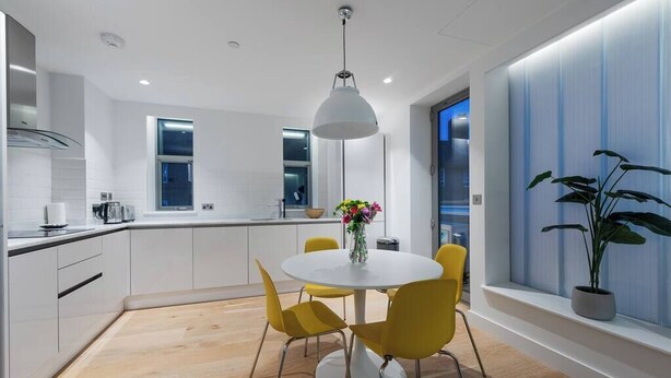 Une cuisine moderne avec des meubles blancs, une table de salle à manger ronde entourée de chaises jaunes et un luminaire suspendu.