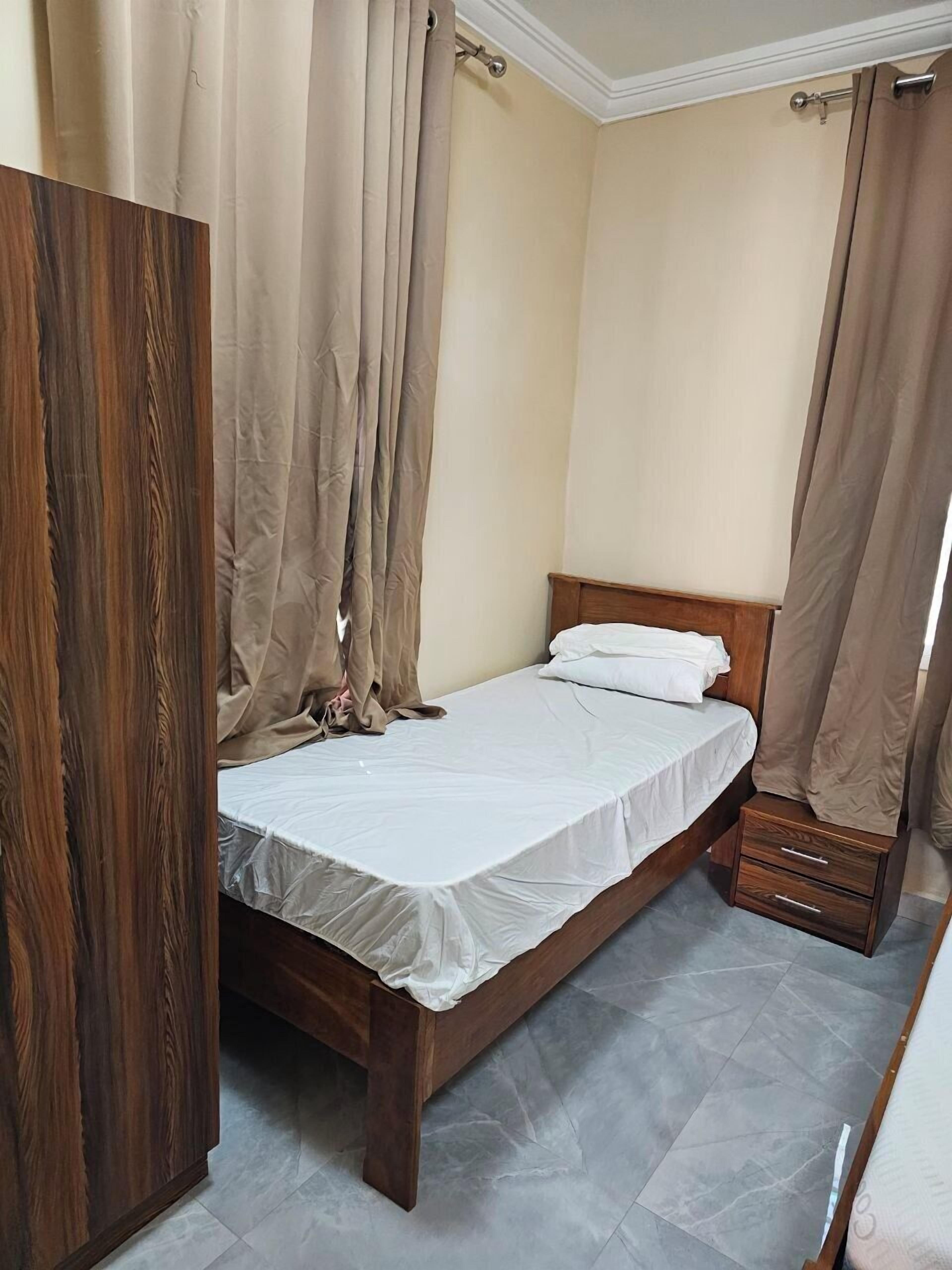 Un dormitorio con una cama de madera, cortinas color beige y un armario de madera.