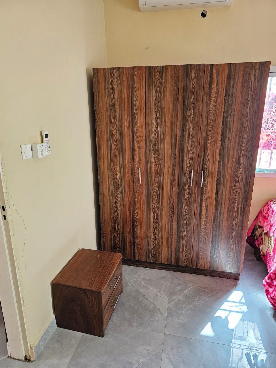 A room with a wardrobe, a small wooden chest, and a tiled floor.