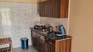 A compact kitchen with dark wooden cabinets, a marble countertop, and a tiled backsplash. - Kaira kunda (Sanyang)