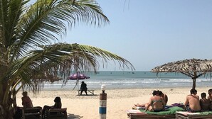 A beach with palm trees, a beach umbrella, and people relaxing on the sand. - Kaira kunda (Sanyang)