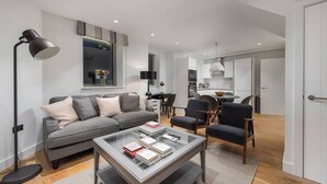 A modern living room with a grey sofa, a glass coffee table, and a desk with a chair. - PBC | Duplex Two Bedroom Apartment in Shoreditch (London)