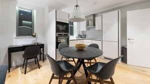 A modern kitchen with white cabinets, a black countertop, and a round dining table with four chairs. - PBC | Duplex Two Bedroom Apartment in Shoreditch (London)