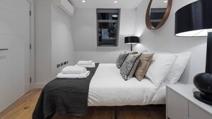 A modern bedroom with a bed, bedside table, lamp, and a mirror on the wall. - PBC | Duplex Two Bedroom Apartment in Shoreditch (London)