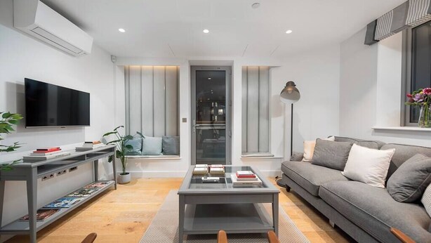 A modern living room with a flat-screen TV, a coffee table, a sofa, and a bookshelf. - PBC | Duplex Two Bedroom Apartment in Shoreditch (London)