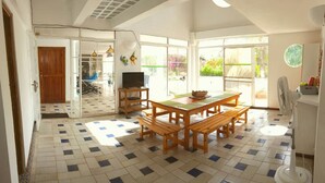 A spacious room with a tiled floor, a wooden dining table with benches, a television on a stand, and a sliding glass door leading to an outdoor area. - Coral house San Andres (San Andrés)