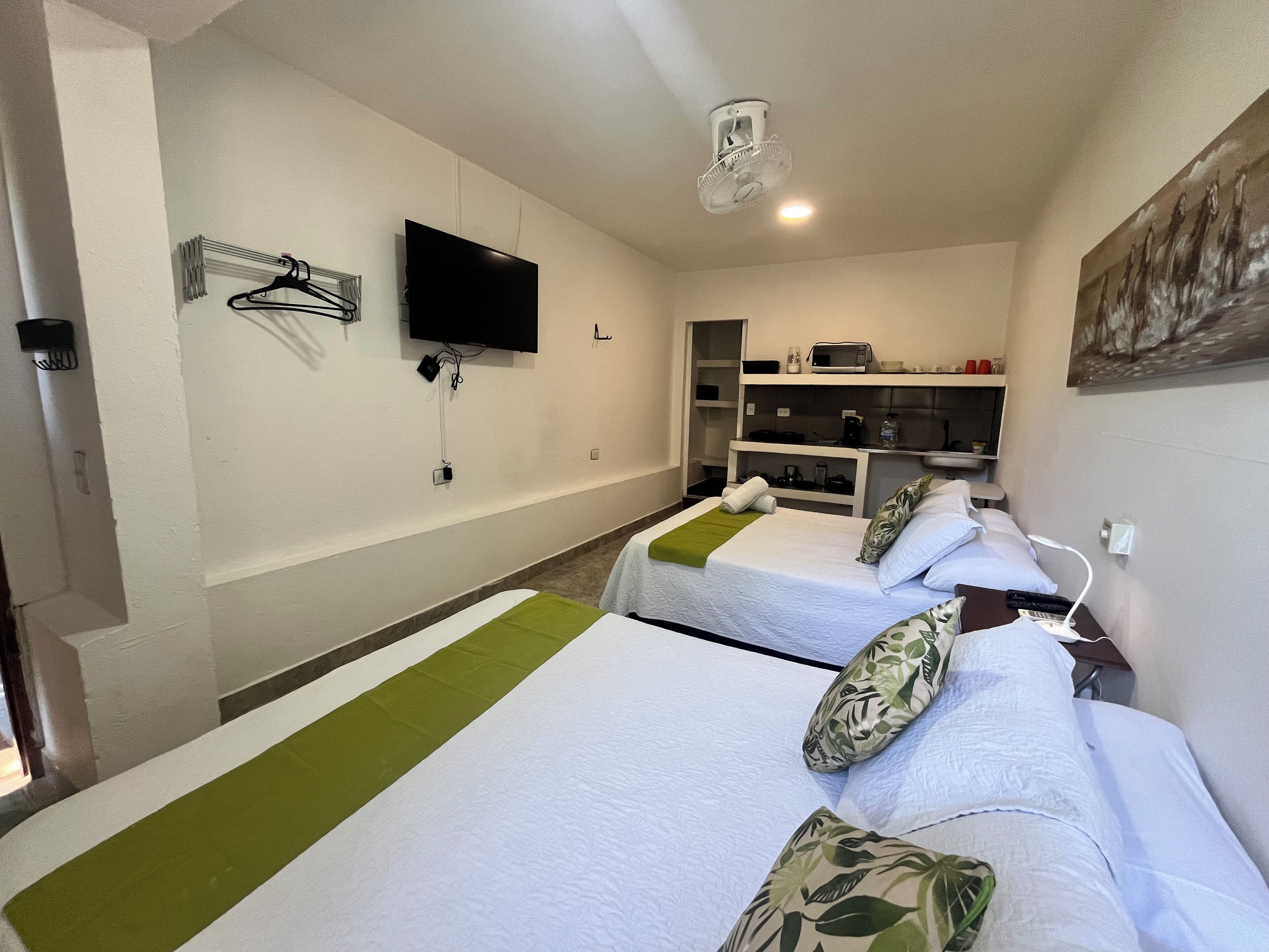 Habitación de hotel con dos camas, televisión, microondas y una pequeña kitchenette.