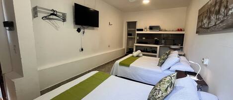 Habitación de hotel con dos camas, televisión, microondas y una pequeña kitchenette.