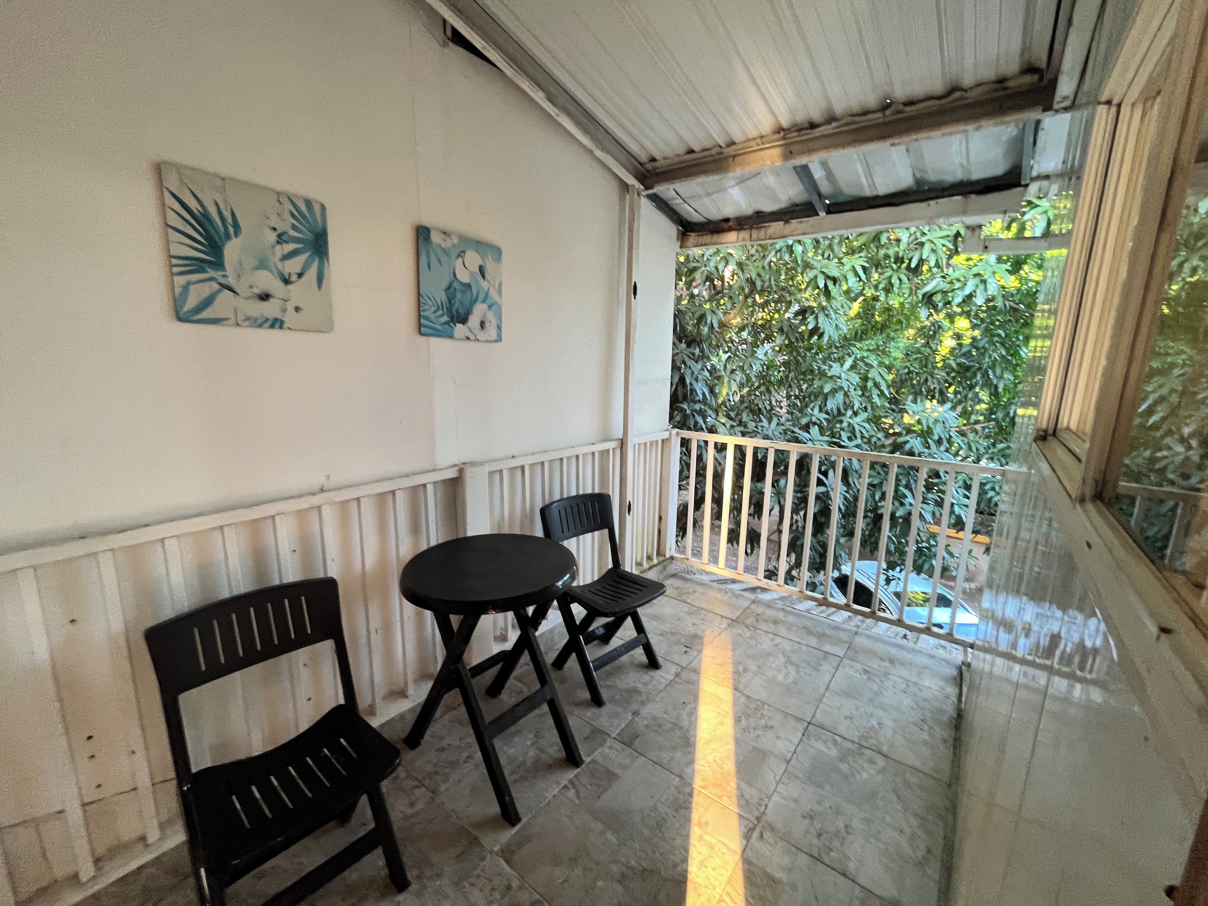 A covered outdoor seating area with a table and chairs, a railing, and artwork on the wall.