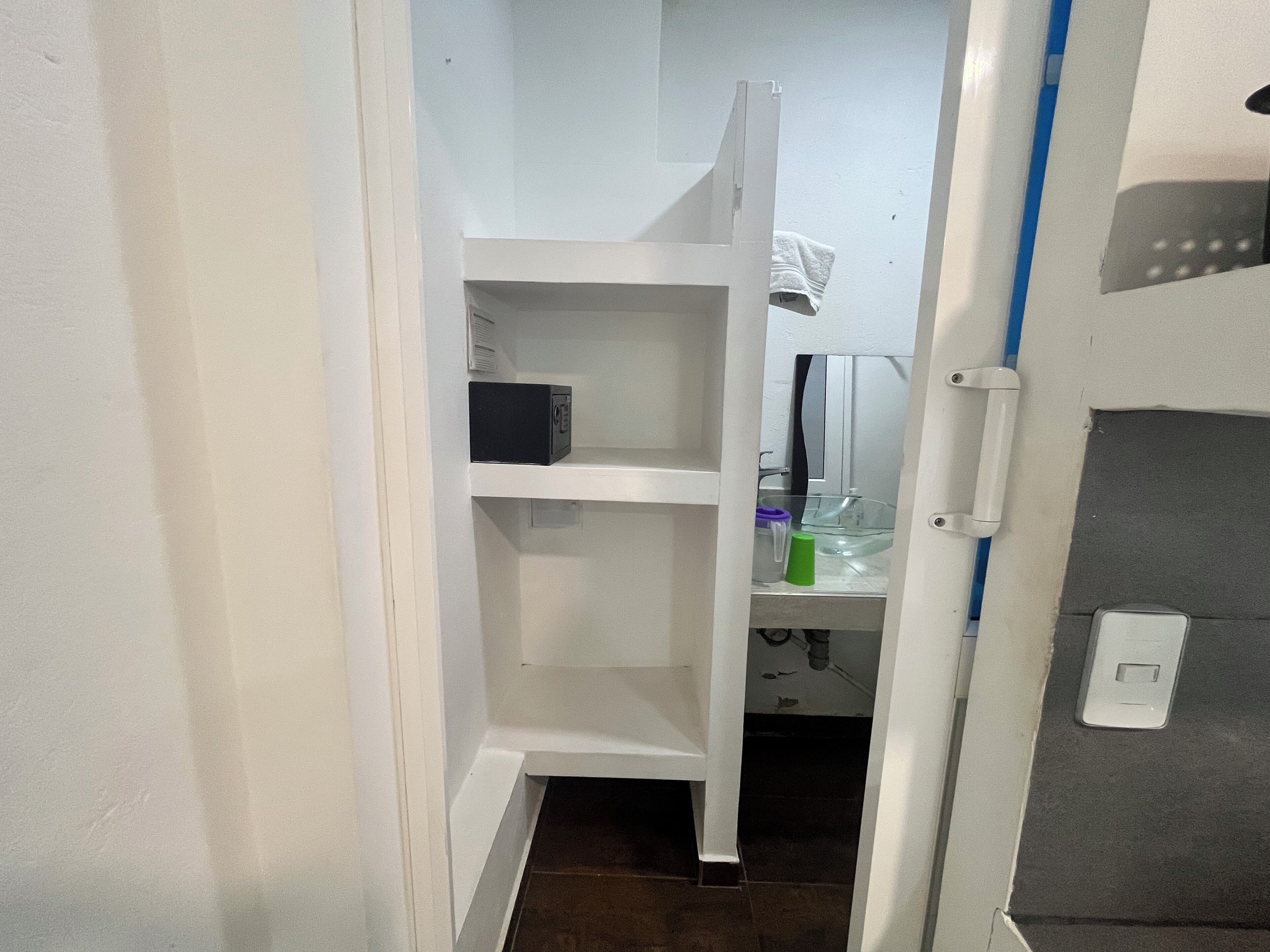A narrow hallway with a white door leading to a room with a small shelf and a microwave.