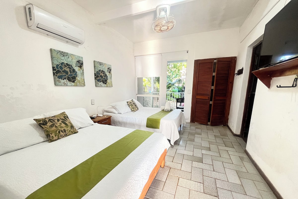 A hotel room with two beds, a ceiling fan, an air conditioner, and a view of the outside.
