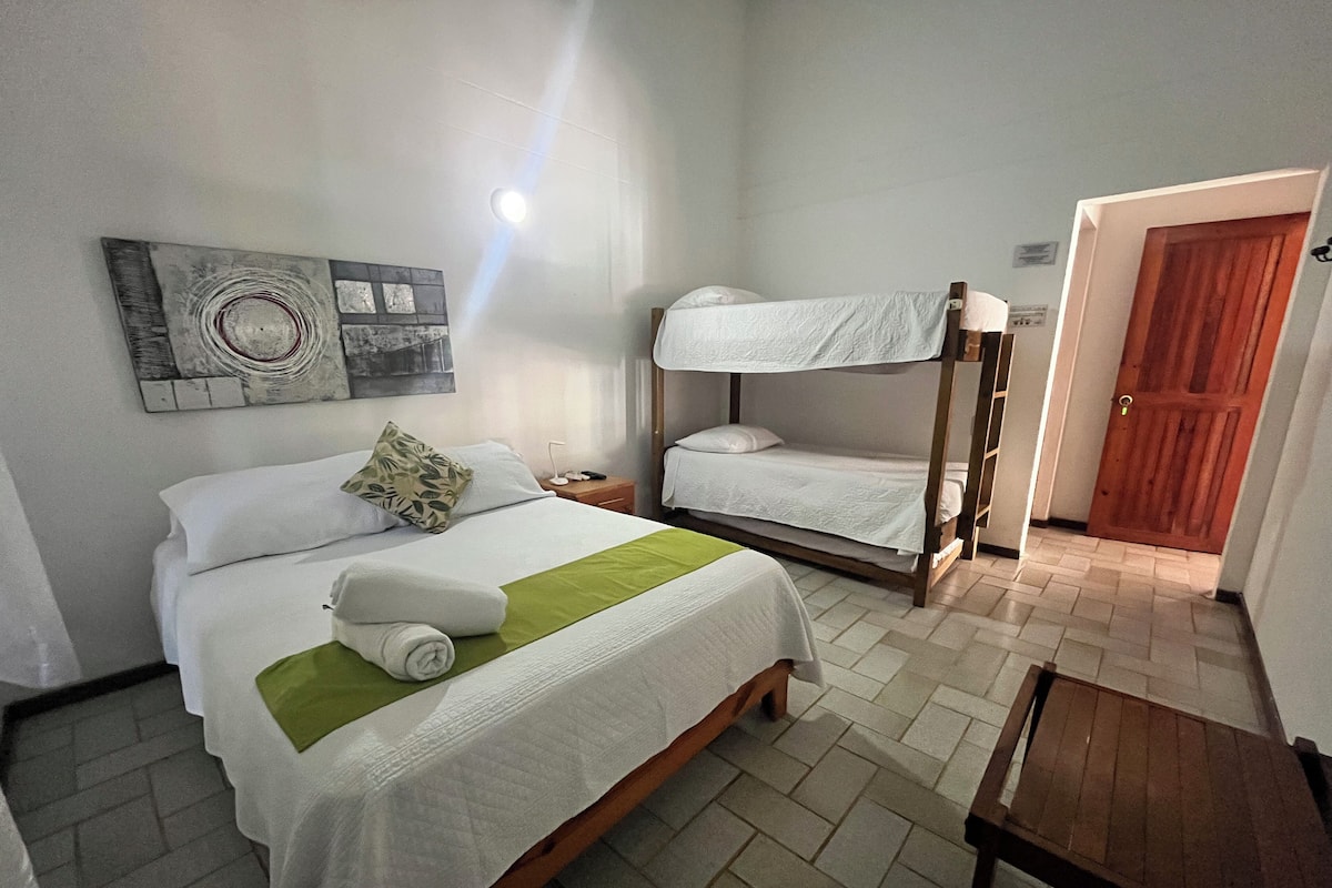 A hotel room with a single bed, a bunk bed, a bedside table, and a wooden bench.