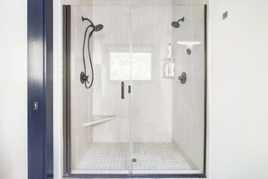 Een douchecabine met glazen wanden, een handdouche, een wandmengkraan en een plank met toiletartikelen.