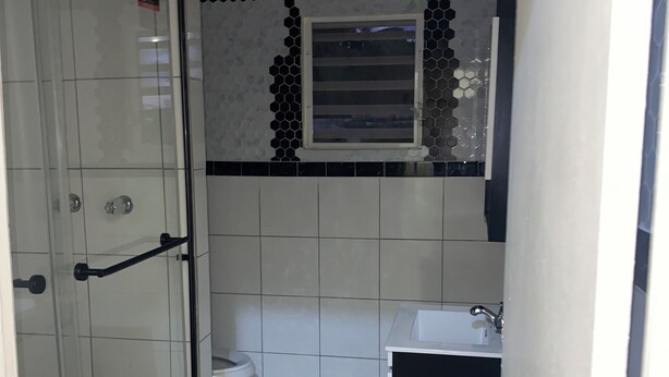 A bathroom with a glass shower enclosure, a toilet, a sink, and a mirror. - D’Emerald of the Sea - Unit 5, Mid-Island 2-Bed Modern Apartment near the Beach (Christiansted)