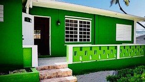 Een groen huis met een witte deur, een raam en een klein portaaltje.