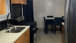 A compact kitchen with a stove, sink, and refrigerator. There is a dining table with chairs and a ceiling fan. - D’Emerald of the Sea - Unit 5, Mid-Island 2-Bed Modern Apartment near the Beach (Christiansted)