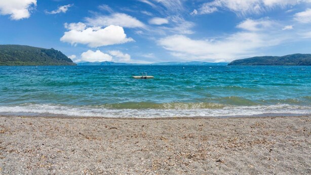 A beach with pebbles, calm water, and distant mountains under a clear sky.