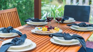 A wooden table set for a meal with plates, napkins, and glasses of red wine.