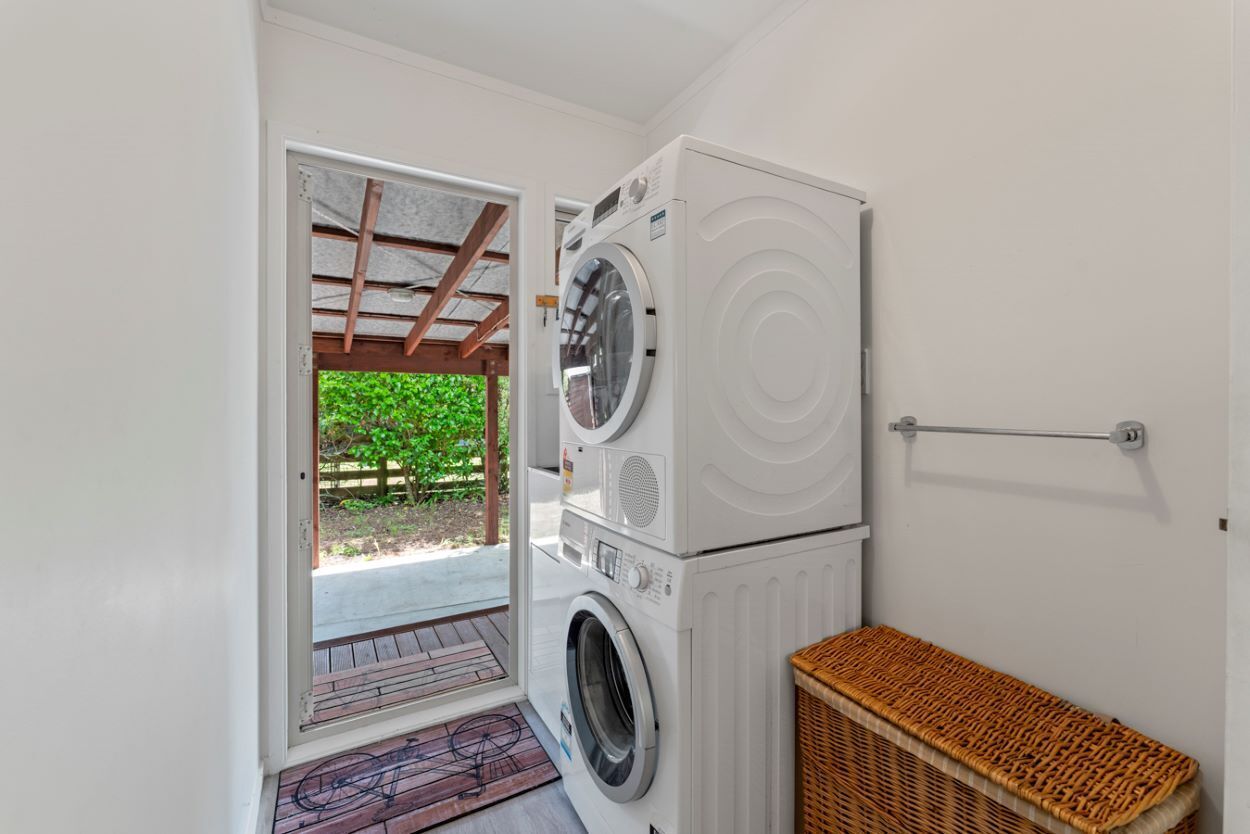 Un cuarto de lavandería con lavadoras apiladas, una cesta de mimbre y una puerta que da a un espacio exterior.