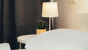 A hotel room with a bed, a nightstand with a lamp, a small cactus, and a wall-mounted light switch. - Beautiful, cozy, family-friendly apartment in the middle of nature. (Sigulda)