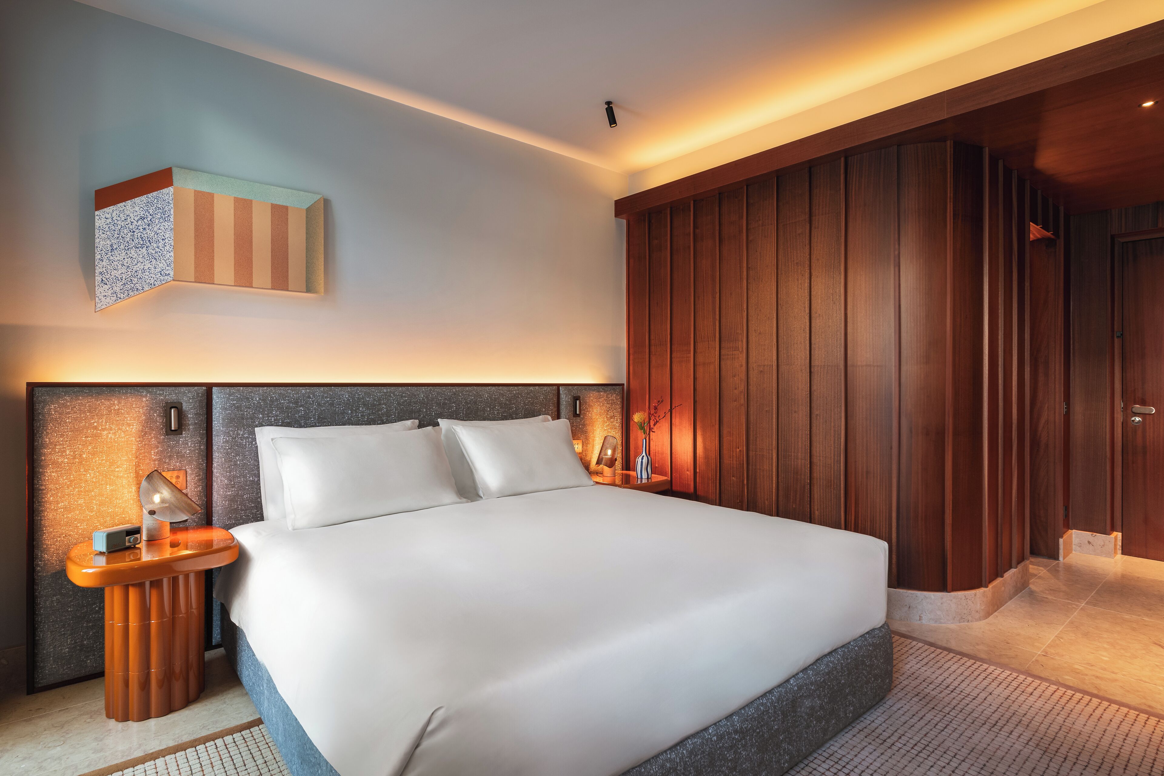 Quarto de hotel moderno com uma cama grande, painéis de madeira e uma obra de arte original na parede.