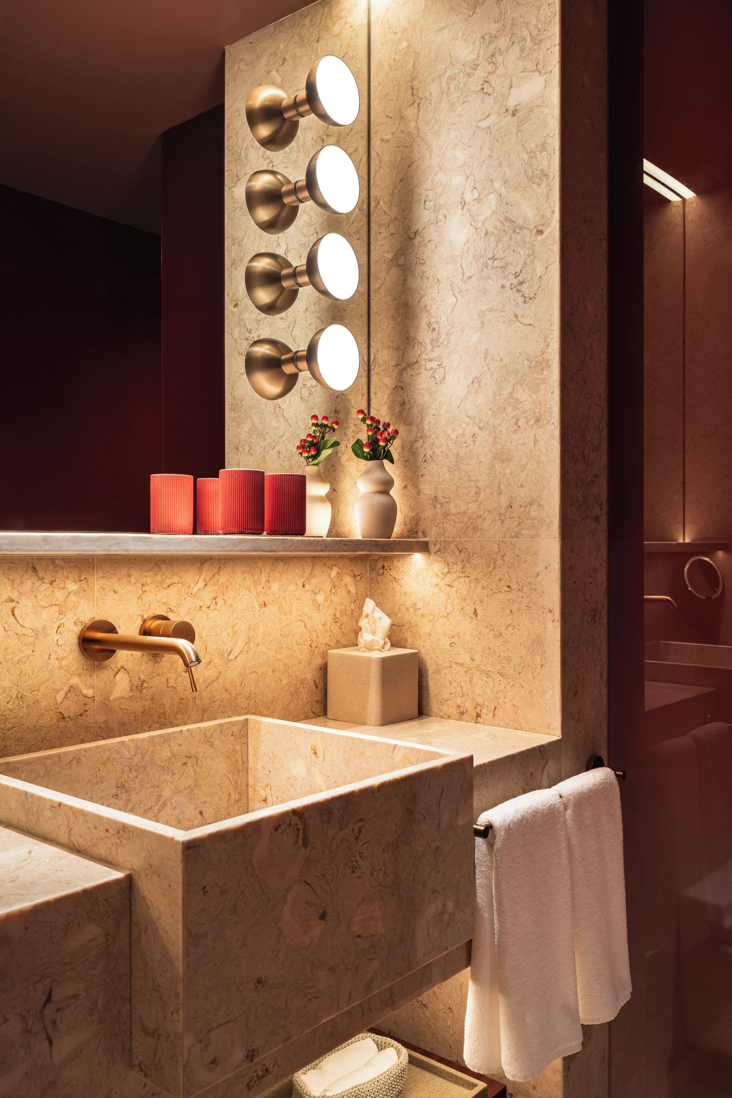 A modern bathroom with a large marble sink, a vanity mirror with lights, and a towel rack.
