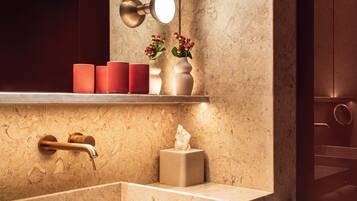 A modern bathroom with a large marble sink, a vanity mirror with lights, and a towel rack.