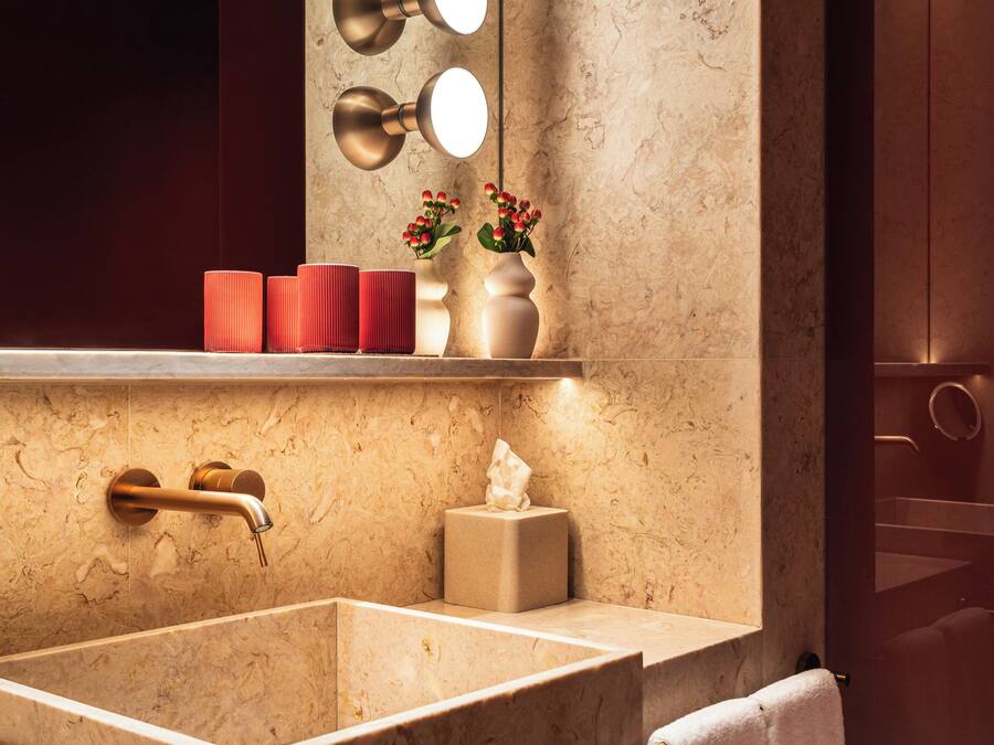 A modern bathroom with a large marble sink, a vanity mirror with lights, and a towel rack.