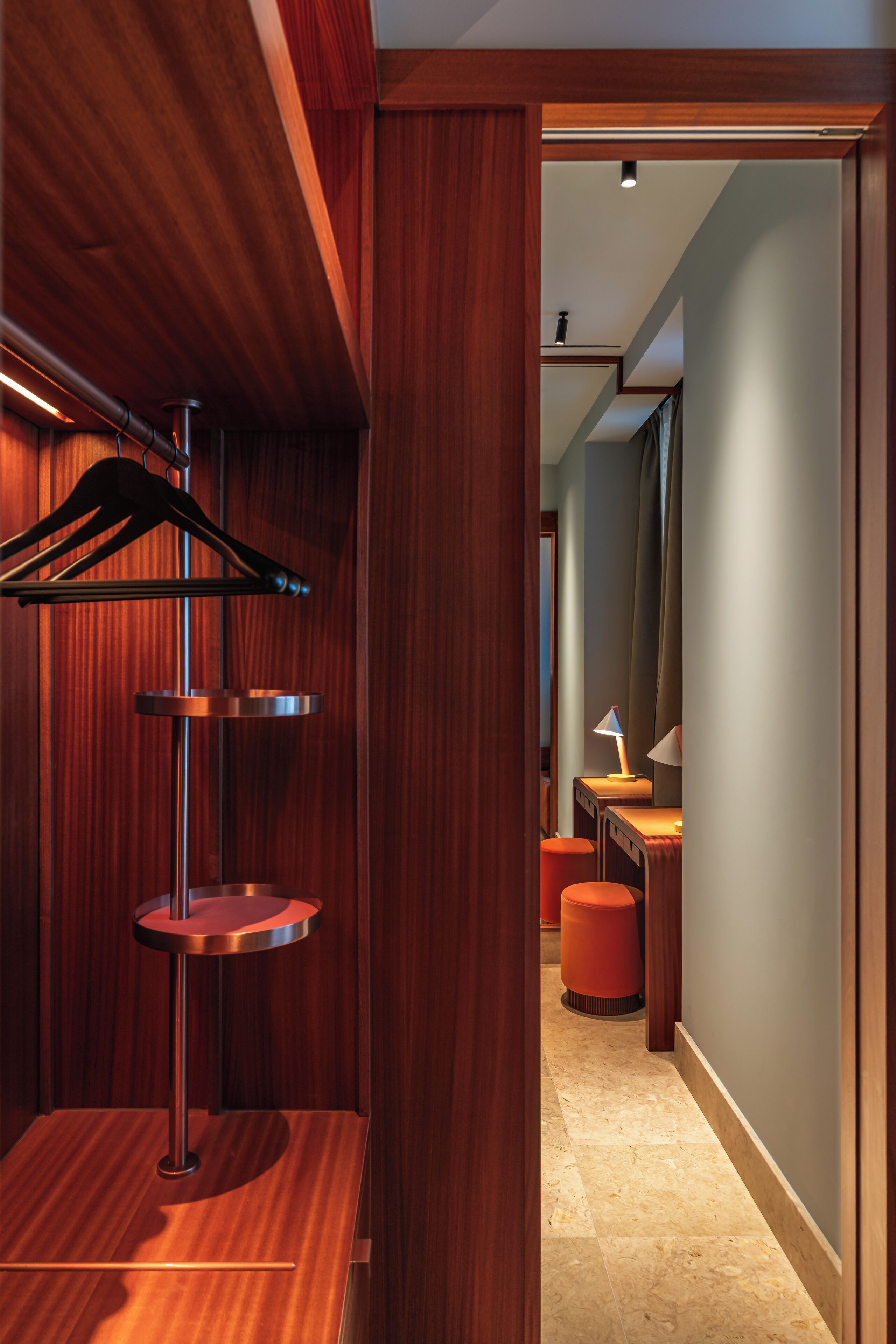 A modern hotel hallway with wooden paneling, a metal coat rack, a round table, and a lamp.