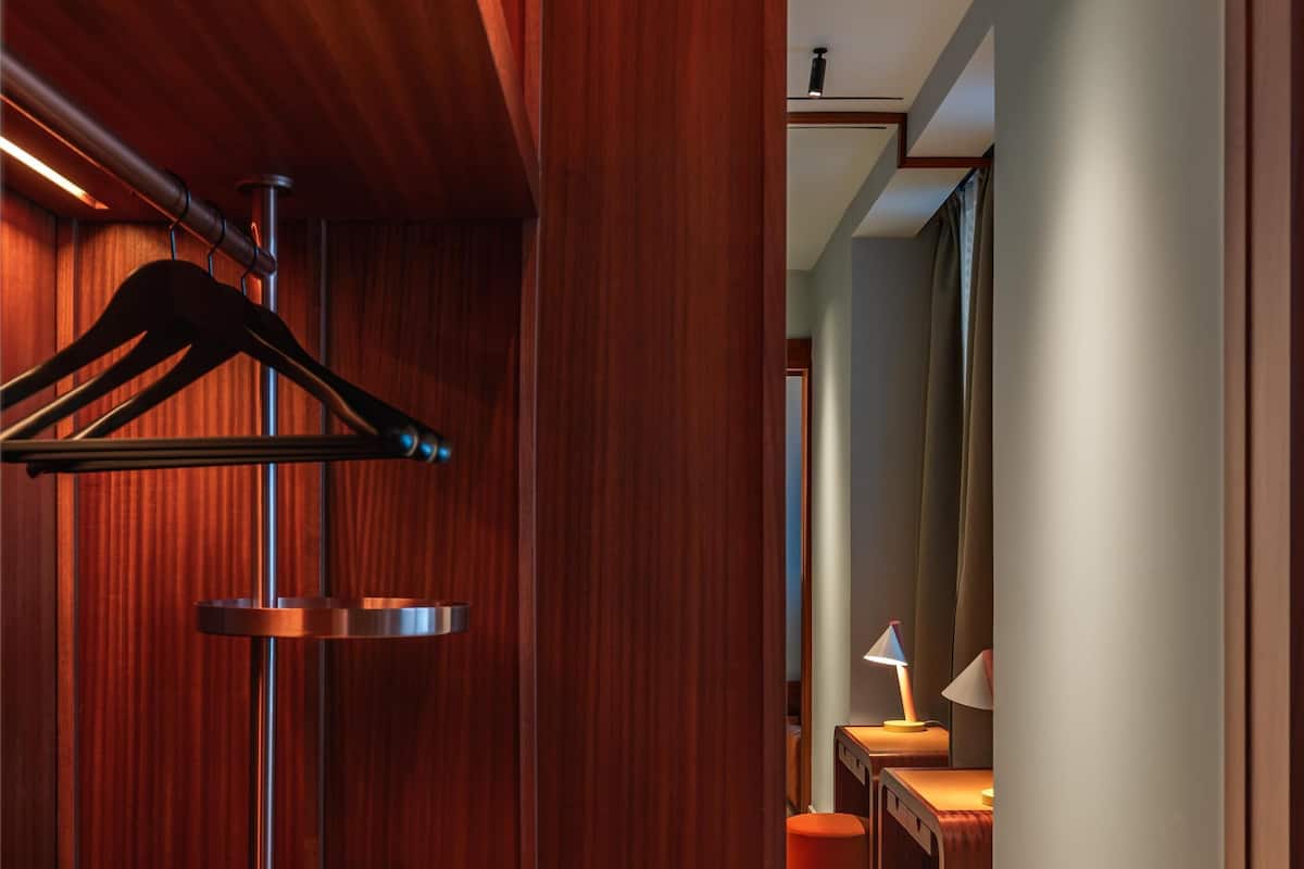 A hallway with wooden paneling, a coat rack, a desk with a lamp, and a trash can.