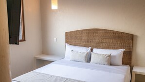 Una cama bien tendida con sábanas blancas y un cabecero tejido, flanqueada por dos mesitas de noche con lámparas.