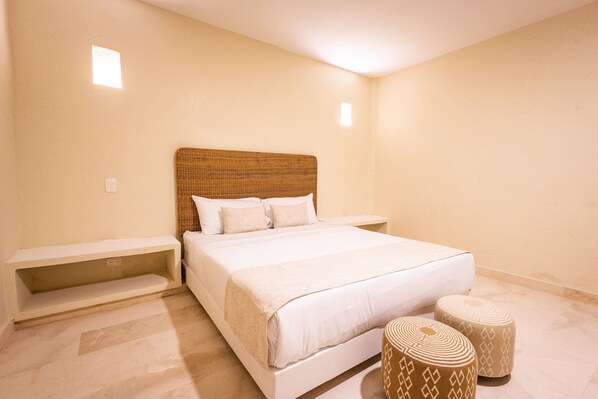A bedroom with a large bed, a headboard, two bedside tables, and two ottomans.