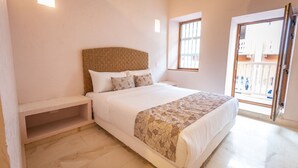 A bedroom with a large bed, a bedside table, a window, and a door leading to an outdoor area.