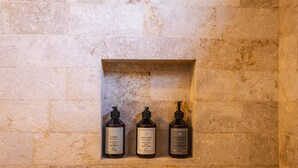 Three bottles of shampoo, body wash, and conditioner in a stone wall niche.
