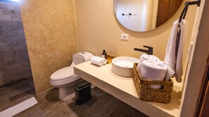 A modern bathroom with a toilet, sink, and mirror. There is a towel rack with towels and a basket of towels.