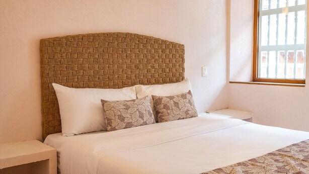 A bed with a woven headboard, white bedding, and patterned pillows.