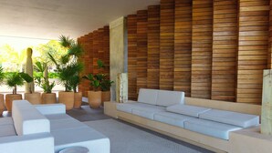 A modern lounge area with a long white sofa, multiple seating options, and potted plants. - Oasis of Beauty (Puerto Vallarta)