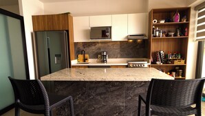 A modern kitchen with a granite island, stainless steel appliances, and wicker chairs. - Oasis of Beauty (Puerto Vallarta)