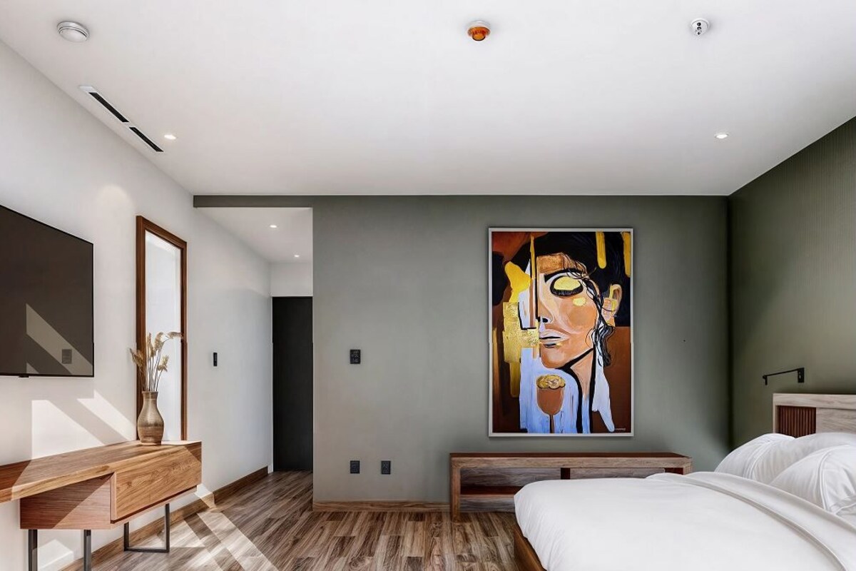 A modern hotel room with a large painting, a wooden desk, and a bed.