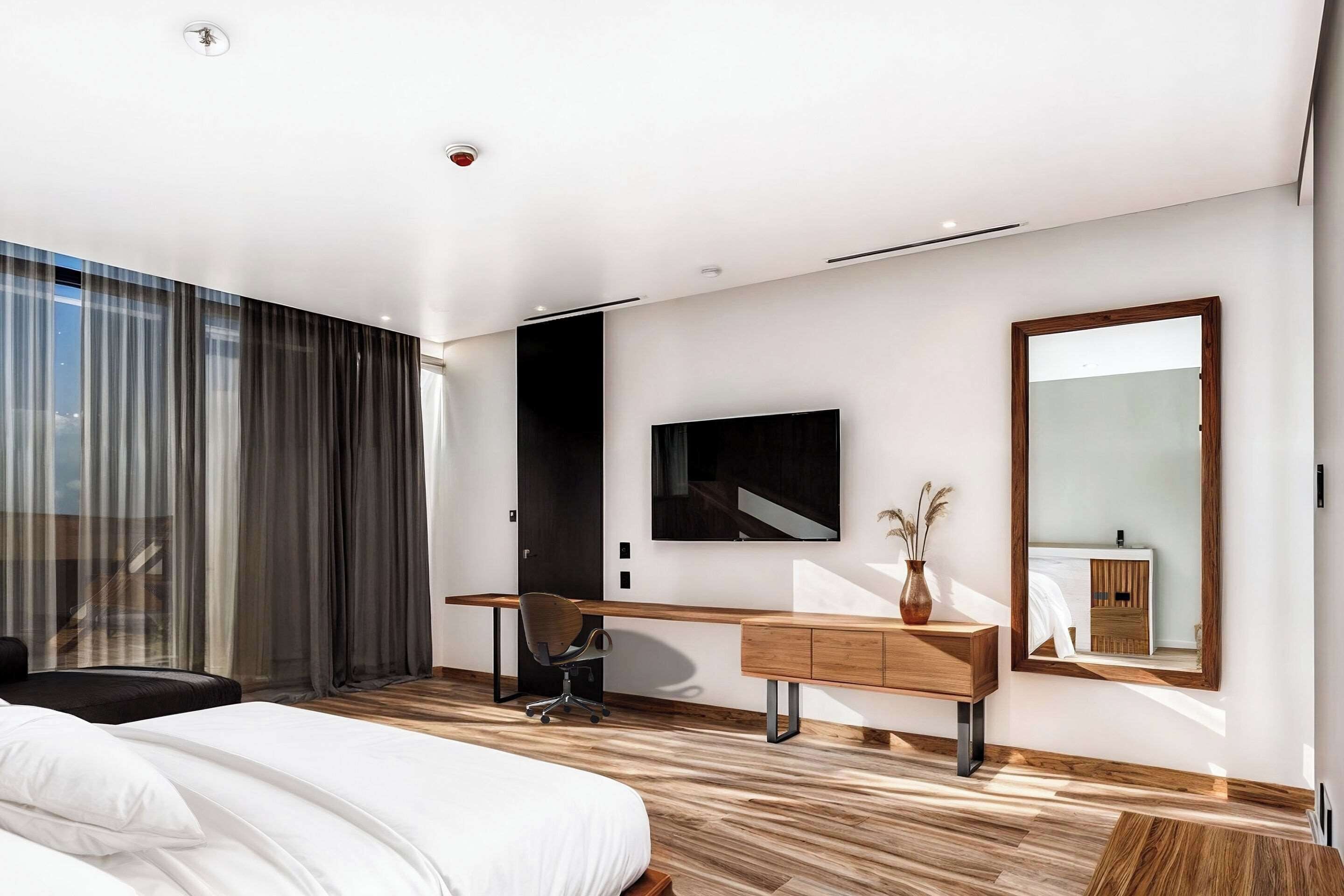 Une chambre d’hôtel moderne dotée d’un grand lit, d’un bureau avec une chaise, d’un grand miroir et offrant une vue sur l’extérieur.