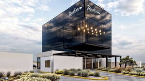 A modern building with the name 'Radisson' on its facade, featuring a glass entrance and a landscaped courtyard with desert plants. - Radisson San Luis Potosi Aeropuerto (San Luis Potosi)