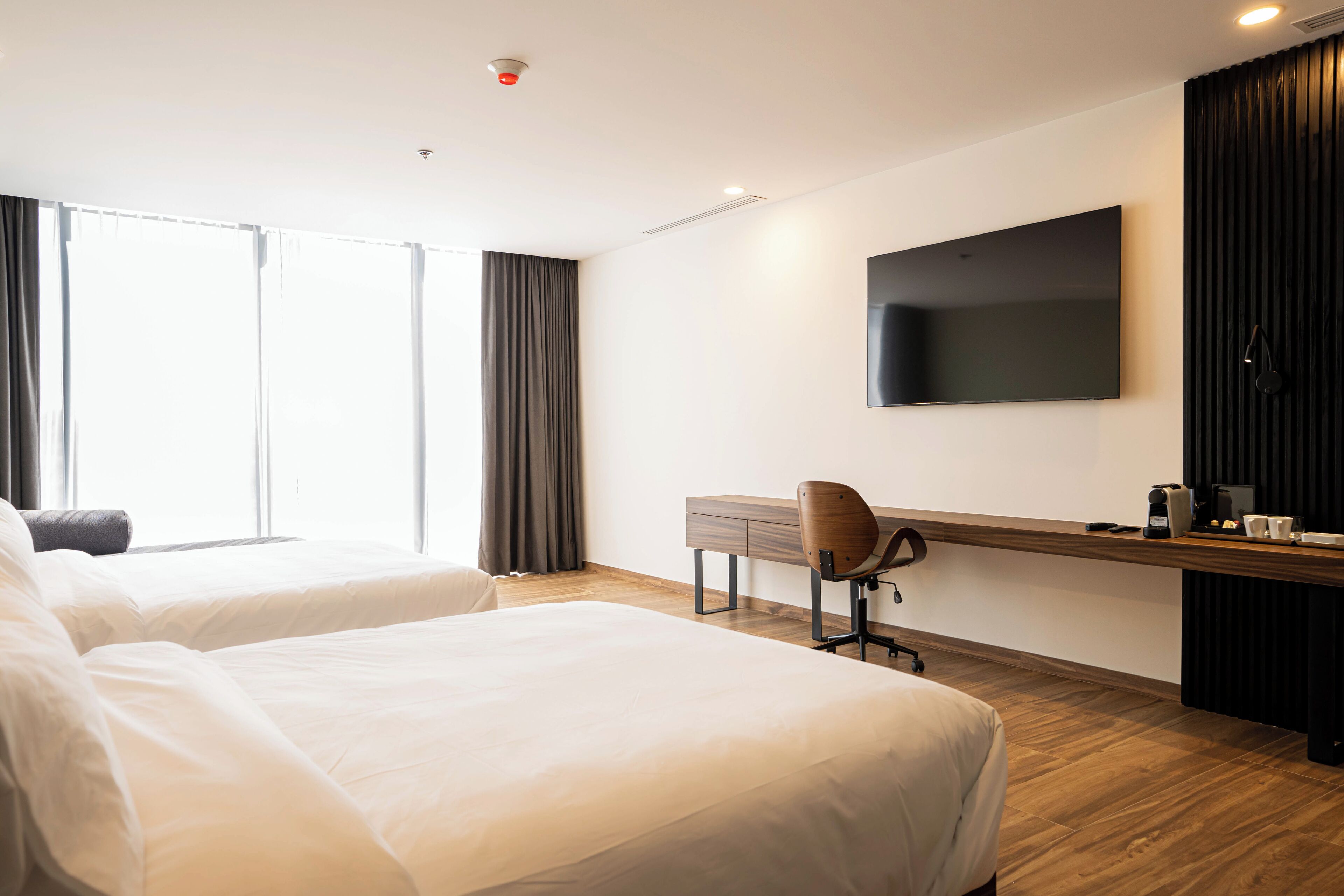 A hotel room with two beds, a desk with a chair, a flat-screen TV, and a coffee machine.