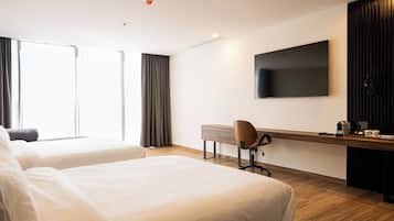 A hotel room with two beds, a desk with a chair, a flat-screen TV, and a coffee machine.