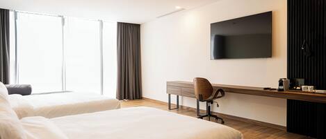 A hotel room with two beds, a desk with a chair, a flat-screen TV, and a coffee machine.