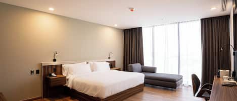 Een moderne hotelkamer met een groot bed, een bureau met stoel, een bank en een groot raam met gordijnen.